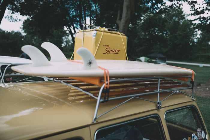 A surfboard and a vintage Squirt cooler strapped to the top of a 1970 Type 3 Squareback Volkswagen Station Wagon seen near turn 3.